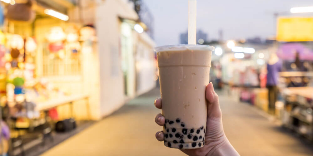 An image of a hand holding a cup of boba tea outdoors