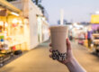 An image of a hand holding a cup of boba tea outdoors
