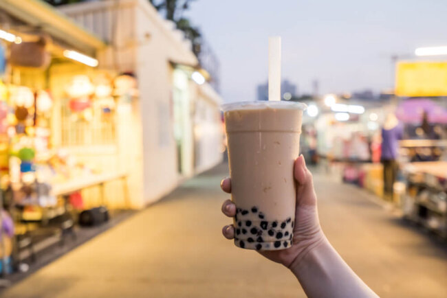 An image of a hand holding a cup of boba tea outdoors